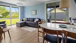 Una sala de estar moderna con un sofá seccional gris, una mesa de comedor redonda con sillas, y un ventanal que ofrece vistas al exterior.