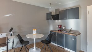 Cocina compacta con una mesa redonda blanca y dos sillas negras, una cafetera y armarios grises.