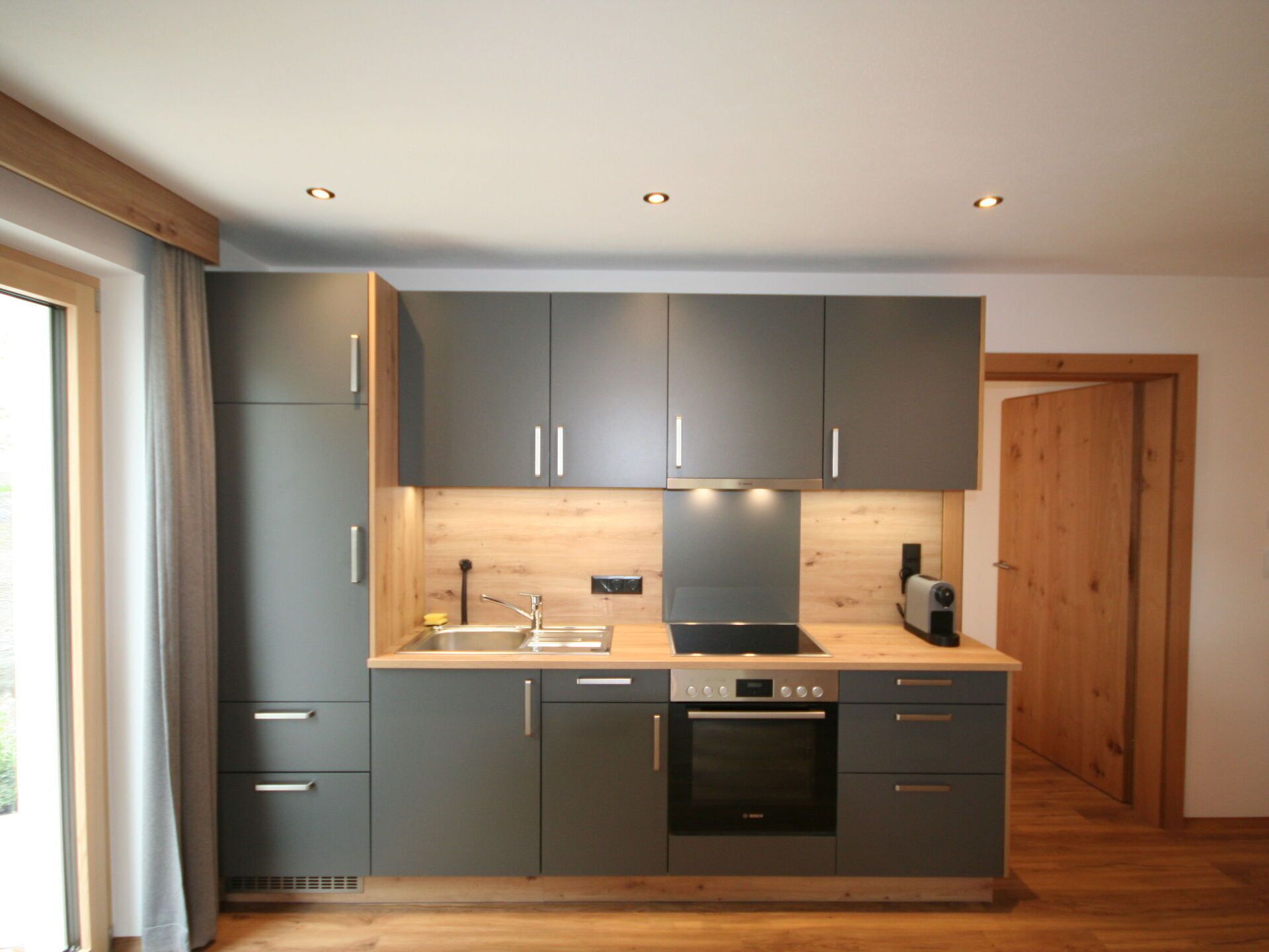 Una cocina moderna con armarios grises, encimera de madera y horno integrado.