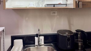A kitchen with a black countertop, a stainless steel sink, a coffee maker, and a cabinet above the sink with glassware. - Stunning skyline views in Makati (Makati)