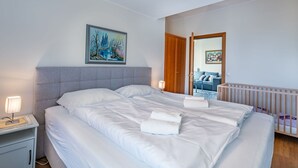 A neatly made bed with white linens and towels, a bedside lamp, a framed painting on the wall, and a wooden door leading to another room. - Nice apartment for 5 people with WIFI, balcony and panoramic view (Frauenstein)