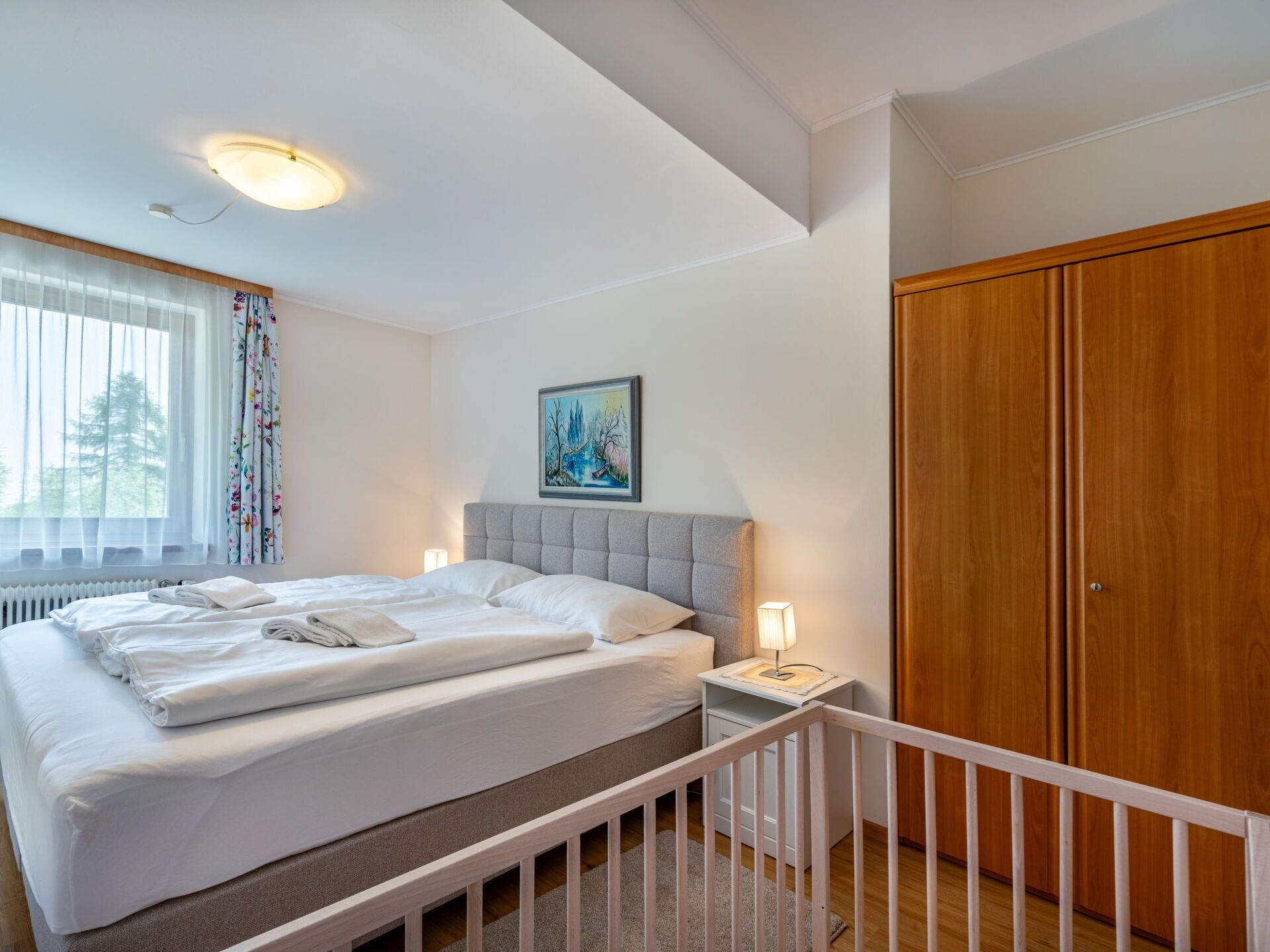 A neatly made bed with white linens, a bedside lamp, and a painting on the wall.