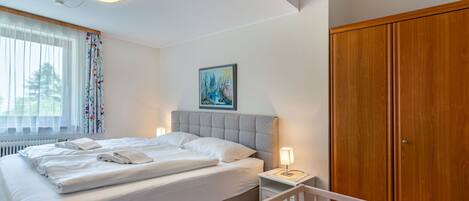 A neatly made bed with white linens, a bedside lamp, and a painting on the wall.