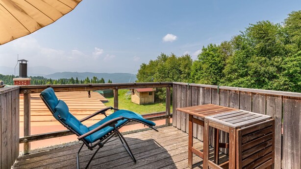 A wooden deck with a blue lounge chair and a small table, overlooking a forested area and distant mountains. - Nice apartment for 5 people with WIFI, balcony and panoramic view (Frauenstein)