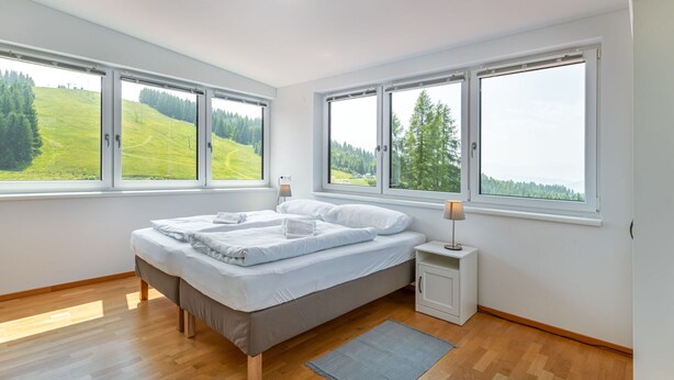 A bedroom with a bed, a nightstand, and a view of a green landscape through large windows. - Lovely apartment for 6 people with WIFI, TV, terrace and panoramic view (Frauenstein)