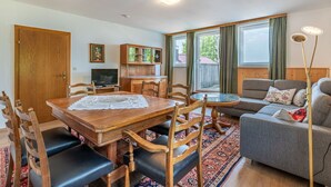 A living room with a wooden dining table, chairs, a sofa, a TV, and a window with curtains. - Lovely apartment for 6 people with WIFI, TV, terrace and panoramic view (Frauenstein)