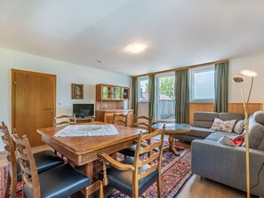 Una sala de estar con una mesa de madera, sillas, un sofá, un televisor y una ventana con cortinas.