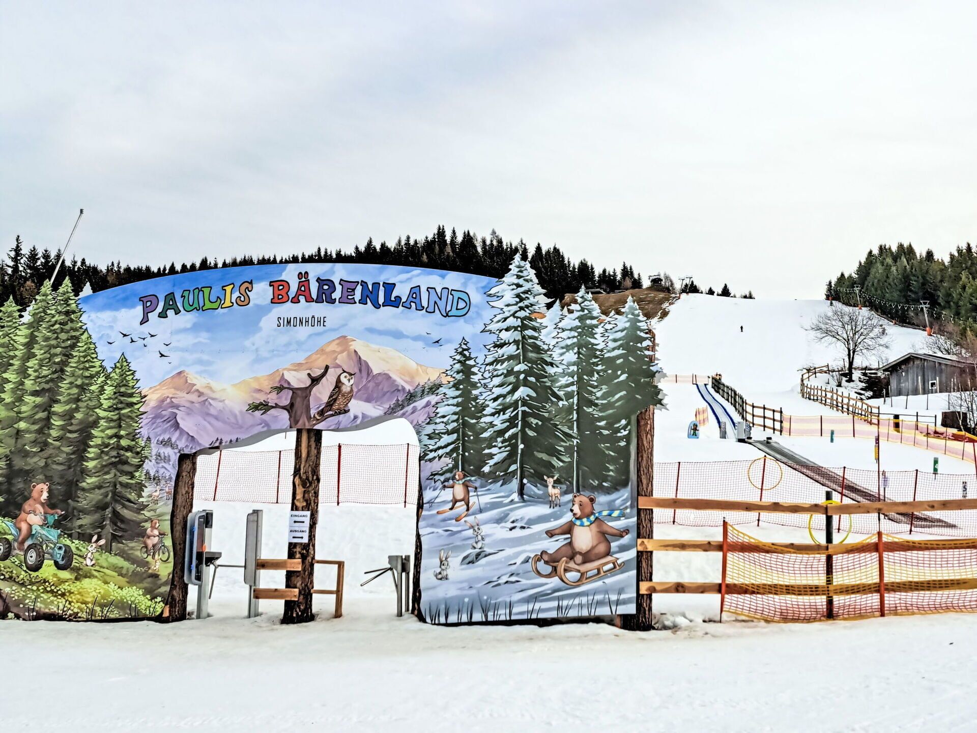 A snowy landscape with a sign reading "Paulis Bärenland" and a ski lift in the background.