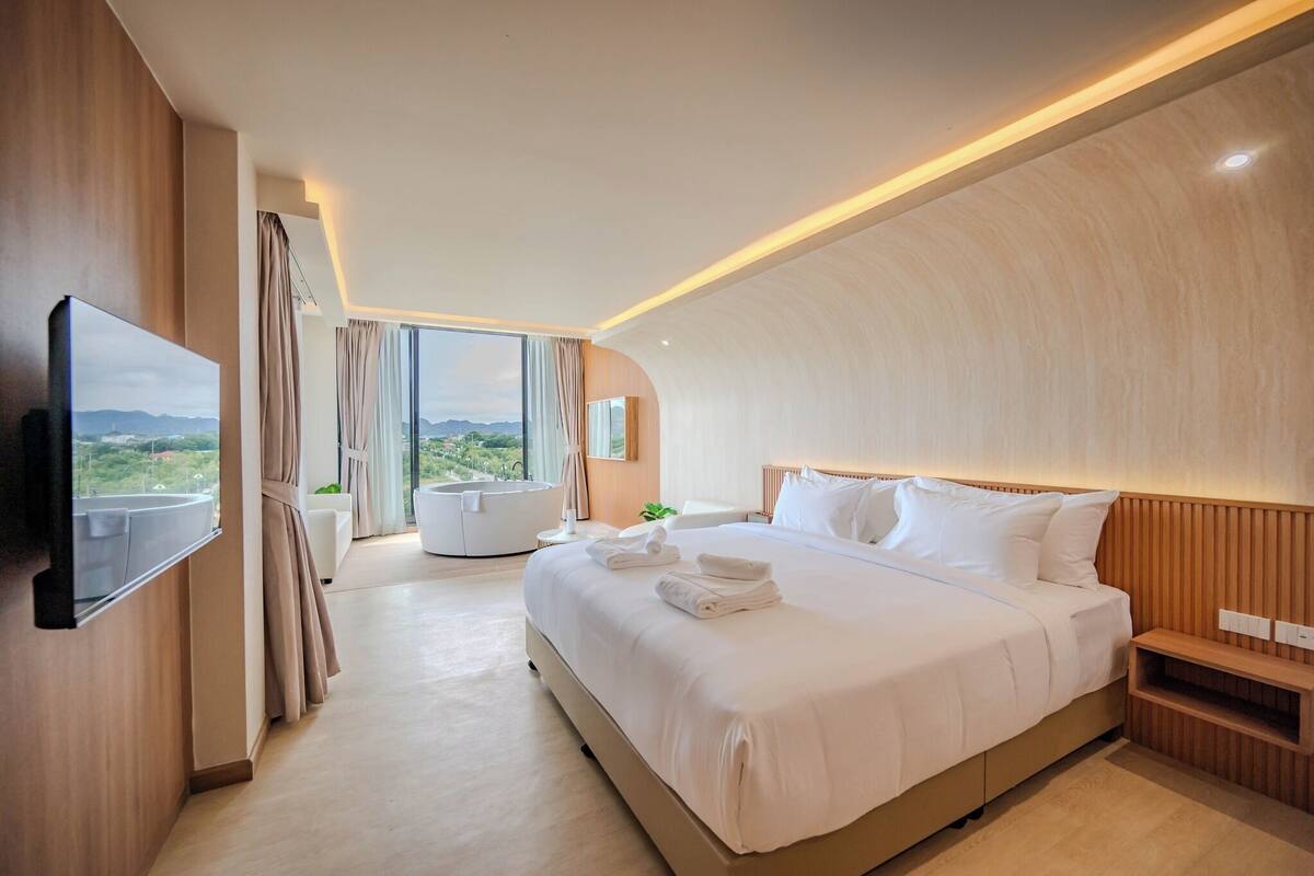 Una moderna camera d'hotel con un letto grande, una TV a schermo piatto fissata al muro, vista sull'esterno e un design del soffitto a volta.