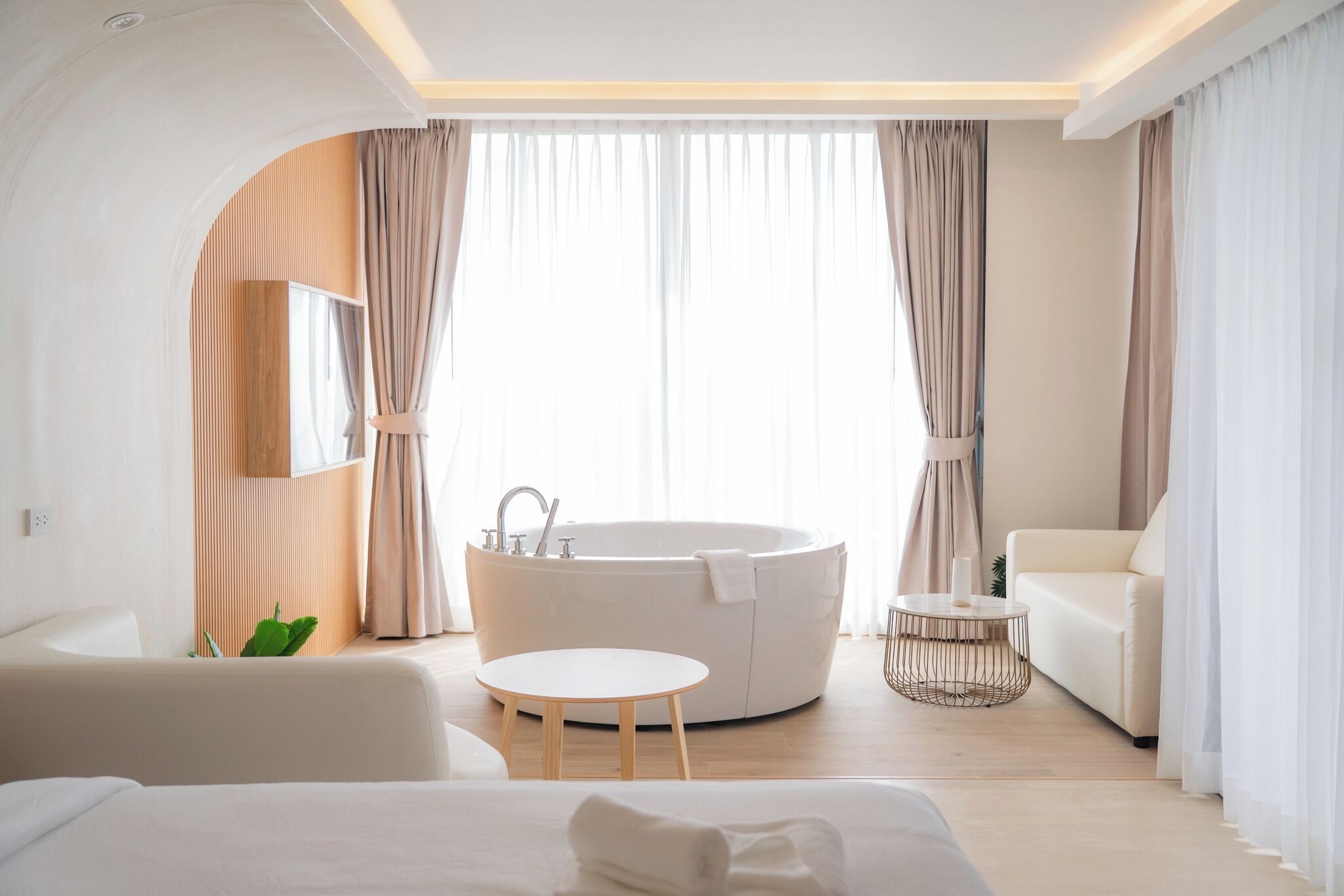 A modern hotel room with a large bathtub, a round table, a sofa, and a bed.
