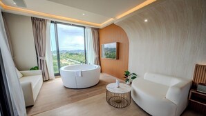 Een moderne woonkamer met een groot raam, een rond zitgedeelte en een flatscreen televisie aan de muur.