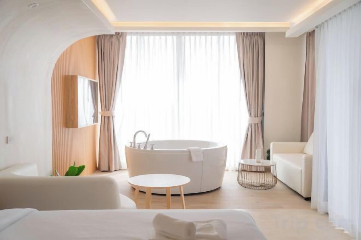 A modern hotel room with a large bed, a round seating area, a bathtub, and a sofa.