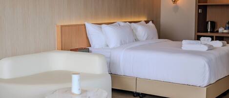 A modern hotel room with a bed, a sofa, a small round table, and a wall-mounted shelf with a kettle.