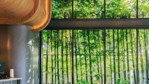 Een modern interieur met een houten bank, grote ramen en uitzicht op bamboe.