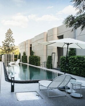 A modern outdoor pool area with a concrete building, lounge chairs, and umbrellas. - G9 Hotel Kanchanaburi (Kanchanaburi)