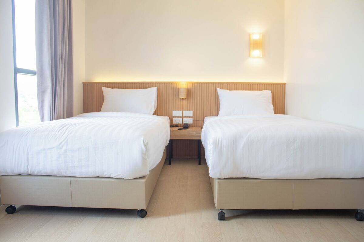Una camera d'albergo con due letti singoli, un comodino, una lampada e un punto luce a parete.