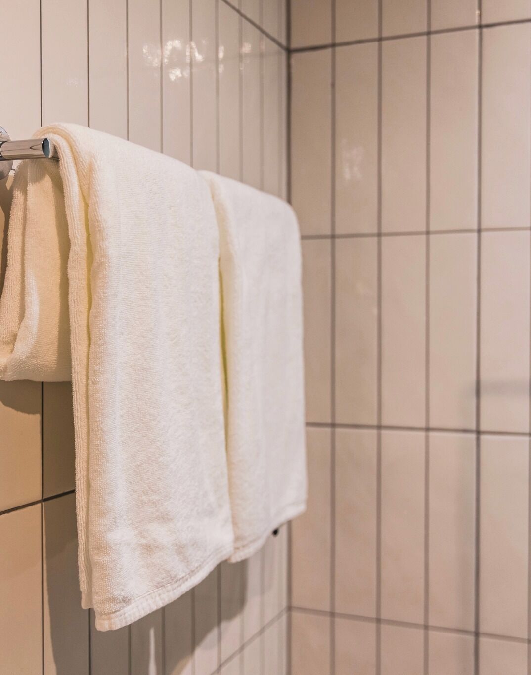 Una toalla blanca colgada en un perchero metálico en un baño con paredes de azulejos.
