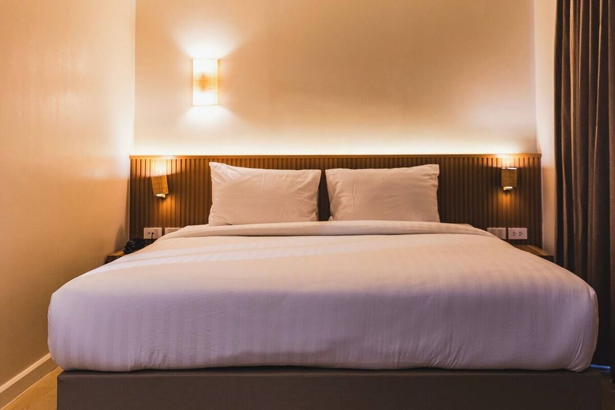 Camera d'albergo con un letto grande, una testiera illuminata e comodini con lampada da parete.