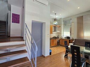Eine moderne Küche mit Holzschränken, ein Essbereich mit einem Glastisch und eine Treppe mit Metallgeländern.