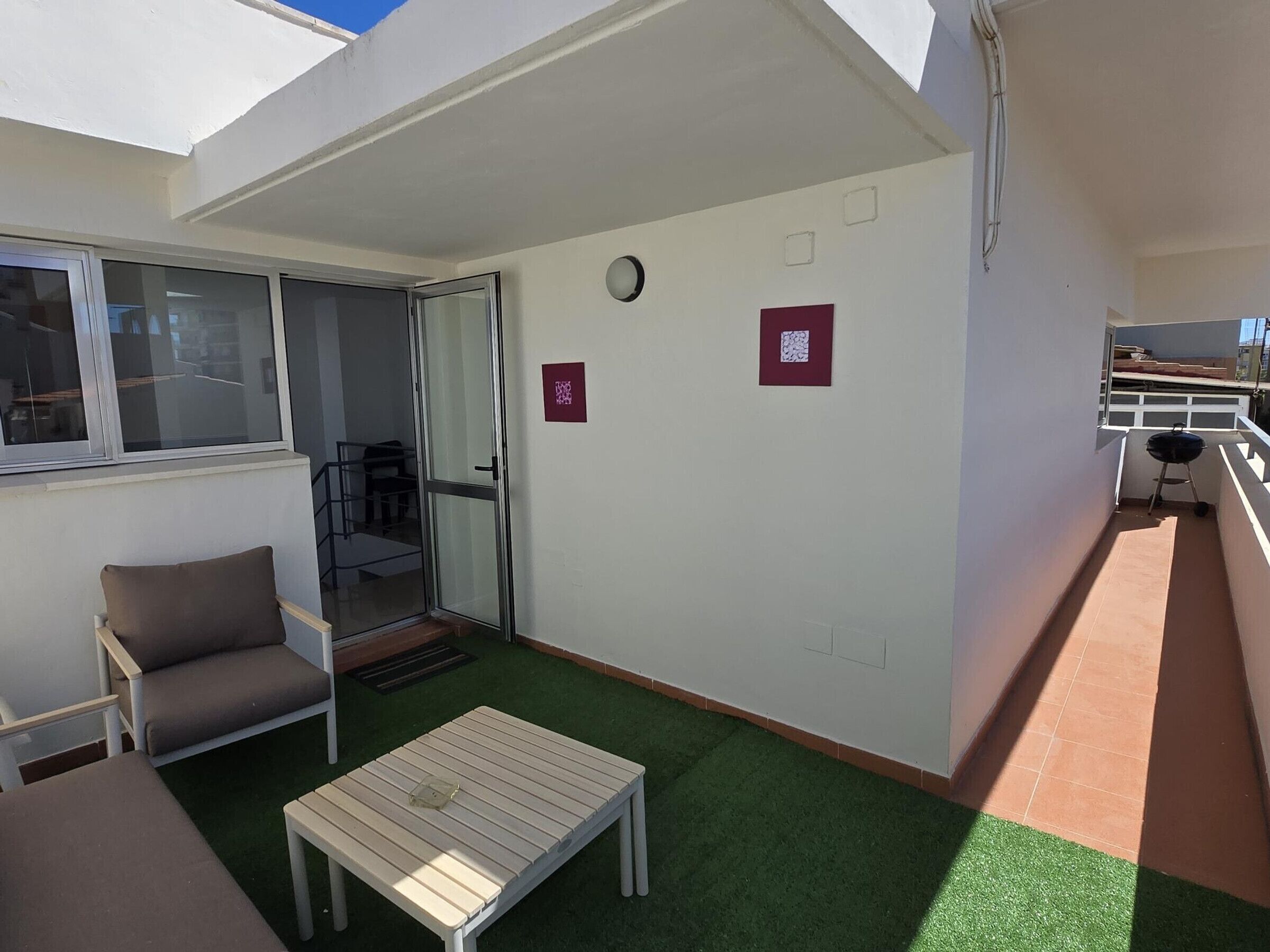 Un balcón con puerta corredera de vidrio, una mesita, una silla y una parrilla.