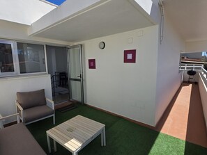 Een balkon met een schuifdeur, een tafeltje, een stoel en een barbecue.
