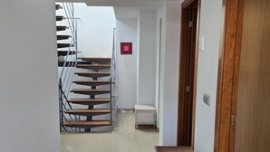 Un pasillo con una escalera de madera, un pequeño banco blanco y una puerta de madera.