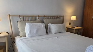 Una cama bien hecha con sábanas blancas, dos almohadas y una toalla enrollada al lado.