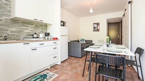 A compact kitchen with white cabinets, a tiled backsplash, and a dining area with a table set for two. - Nice apartment for 5 people with A/C, pool, WIFI and TV (Castelveccana)
