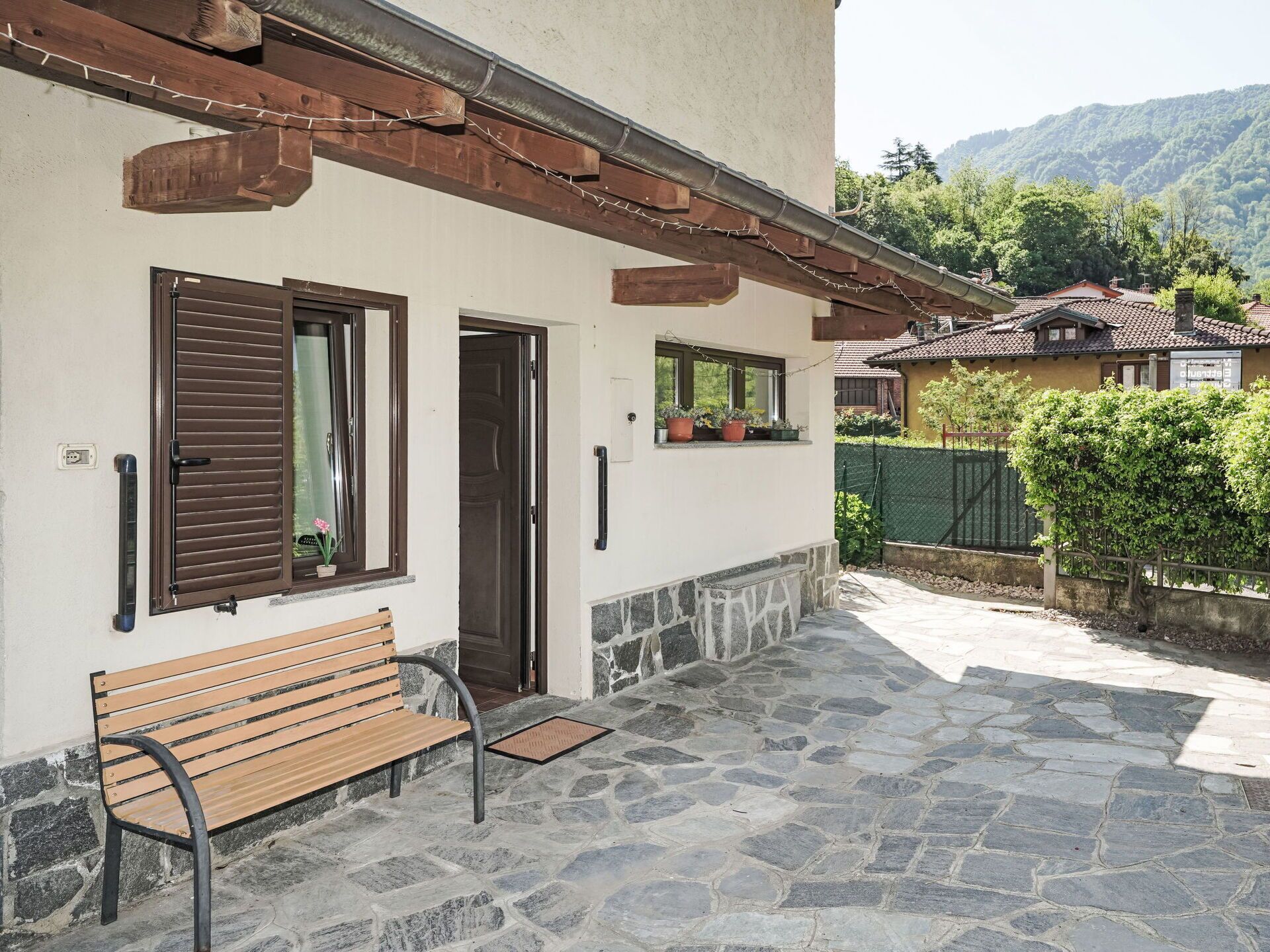 A stone-paved patio with a wooden bench, a door, and windows with shutters.