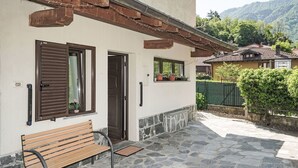 A stone-paved patio with a wooden bench, a door, and windows with shutters. - Nice apartment for 5 people with A/C, pool, WIFI and TV (Castelveccana)