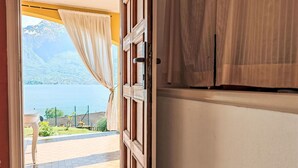 Puerta abierta que da a un balcón con vistas a un lago y montañas.