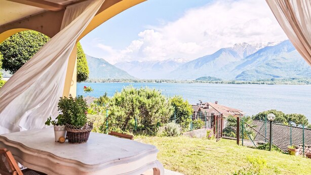 Una terraza con una mesa y sillas, vista a un lago y montañas al fondo.