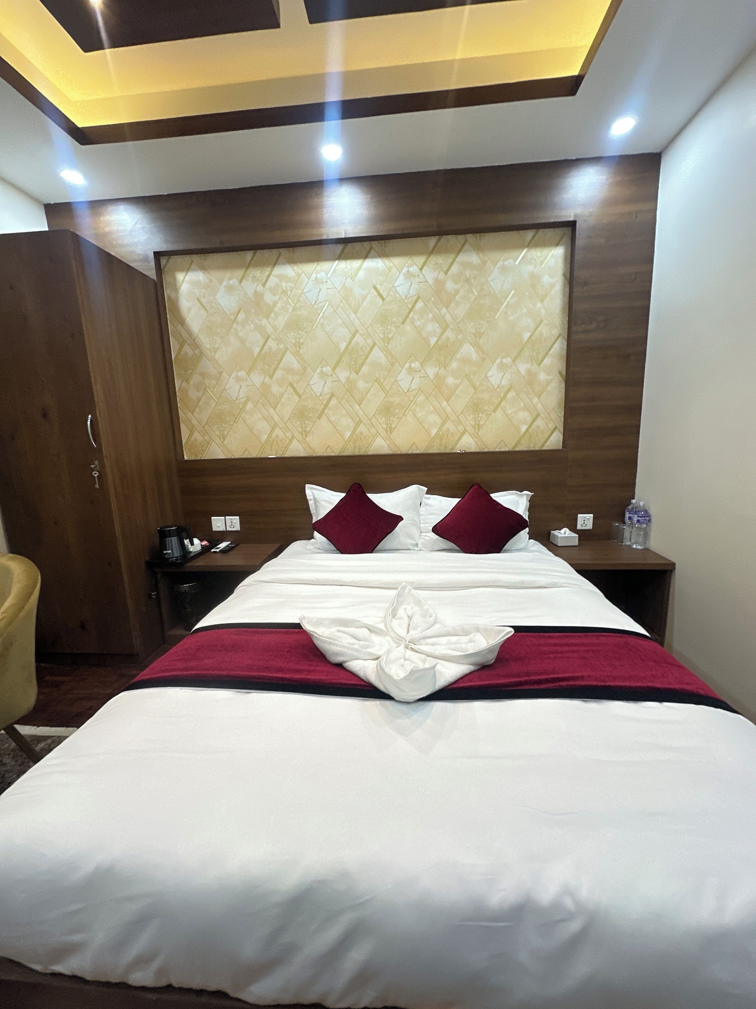 Une chambre d’hôtel avec un lit bien fait, une tête de lit en bois et une table de chevet sur laquelle se trouvent une bouteille d’eau et des mouchoirs.