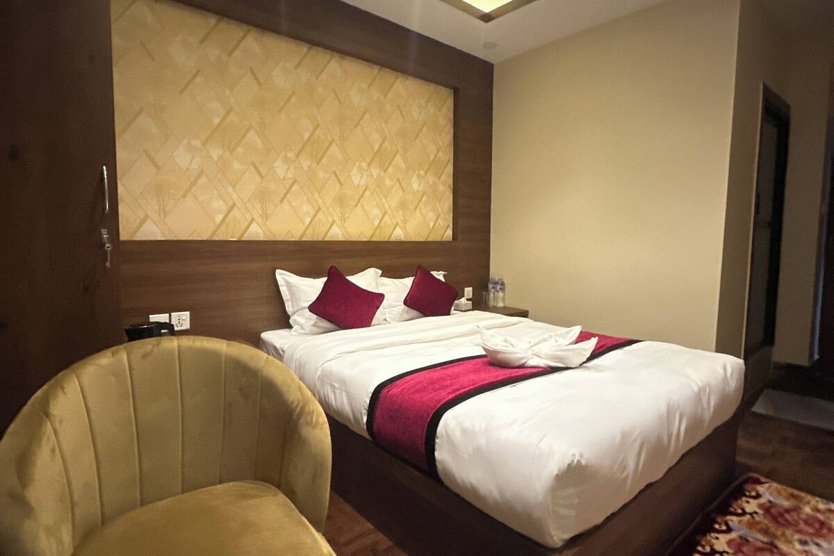 A hotel room with a large bed, a headboard with a geometric pattern, a wooden floor, and a chair.