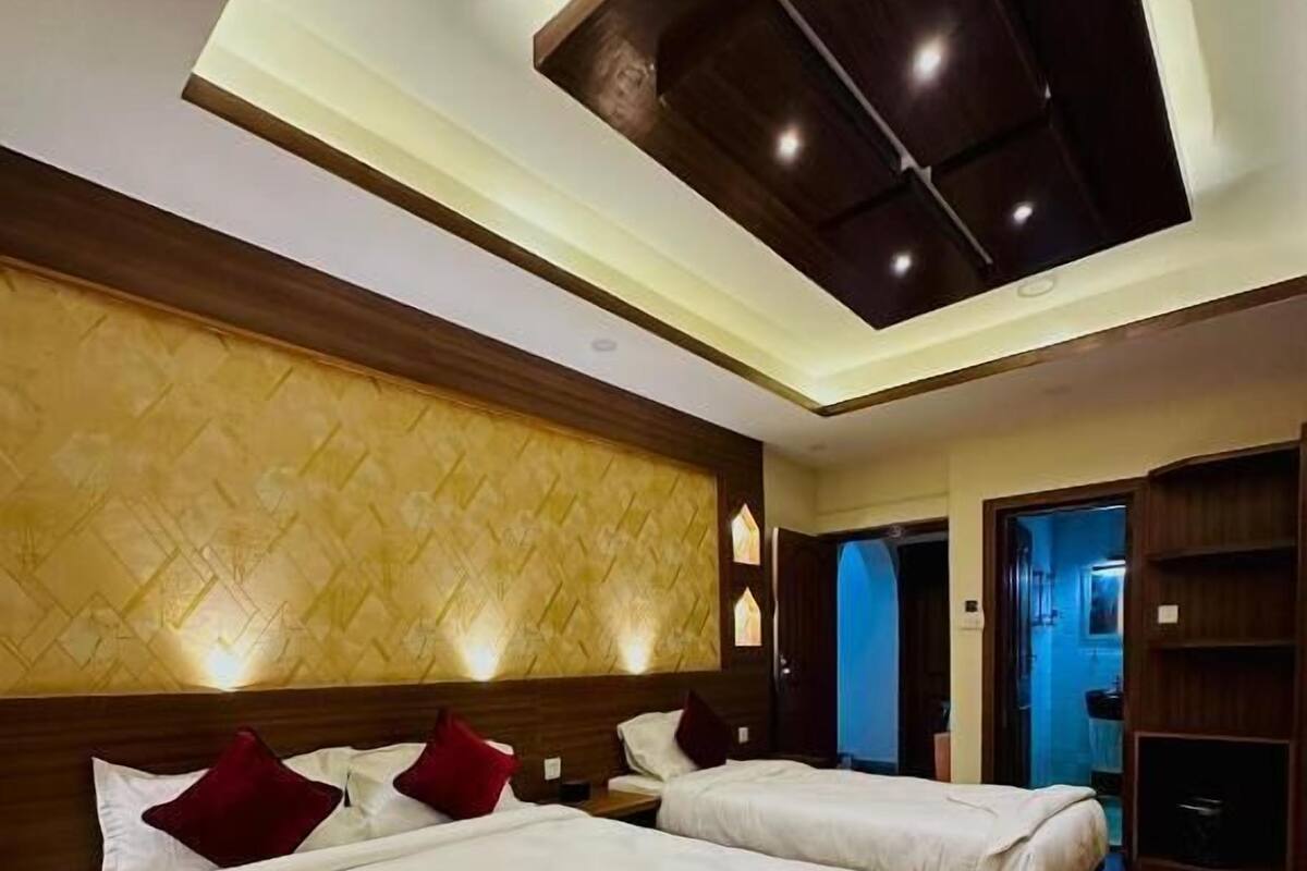 A hotel room with two beds, wooden headboards, a patterned wall, and a ceiling with recessed lighting.