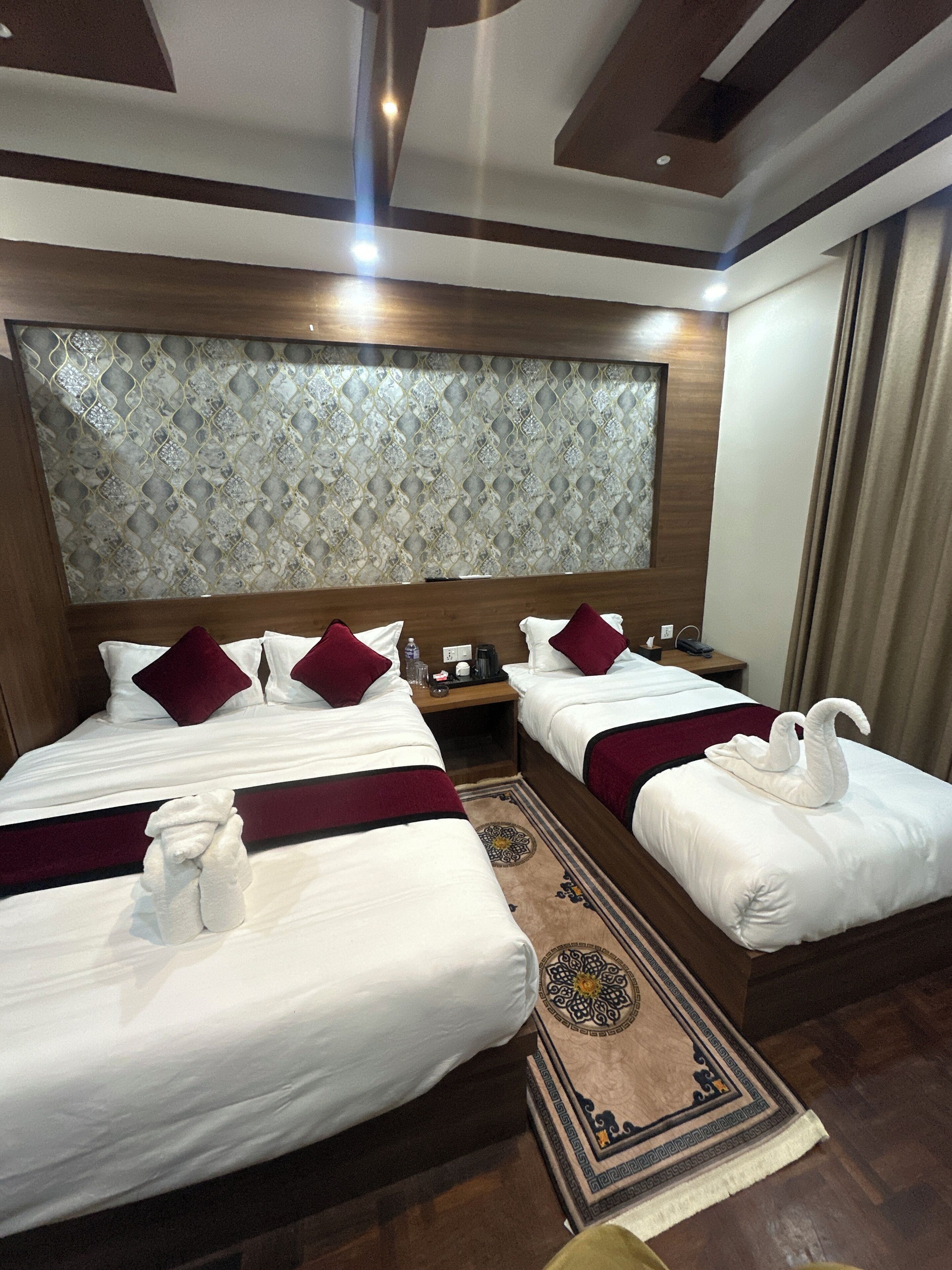 Ein Hotelzimmer mit zwei Betten, jeweils mit weißer Bettwäsche und roten Kissen, einem Holz-Kopfteil und einer dekorativen Wandverkleidung.