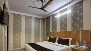 Una habitación de hotel con una cama, una mesita de noche, un ventilador de techo y papel tapiz estampado.