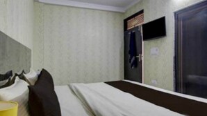 Una cama individual con una colcha blanca y marrón, un almohadón negro y una taza amarilla a la izquierda. A la derecha, se observa una puerta con un ventanal.