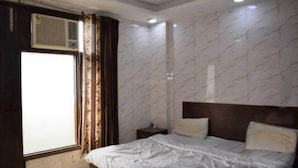 Un dormitorio con una cama, una mesita de noche, una ventana con cortinas y un equipo de aire acondicionado.