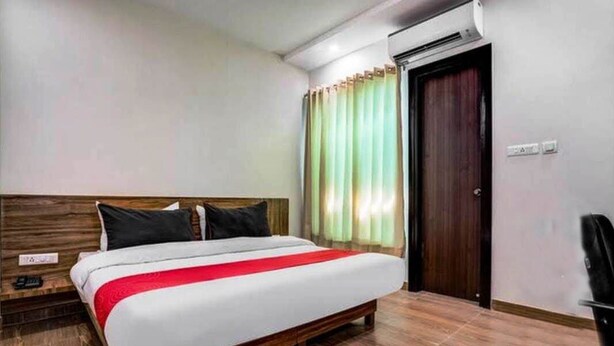 Habitación de hotel con una cama de madera, un plaid rojo, cabecera de madera, cortina verde y un equipo de aire acondicionado.