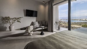 A modern bedroom with a large bed, a TV mounted on the wall, and a view of a rocky coastline through a large window. - Villa Quintessa (Povljana)