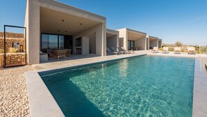 A modern poolside area with a clear blue pool, lounge chairs, and a stone wall backdrop. - Villa Quintessa (Povljana)
