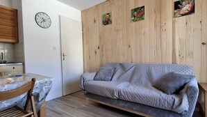 A room with a wooden wall, a grey sofa, a wooden dining table, and a clock on the wall.