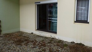 A building with a small window and a door, a balcony, and a gravel ground.