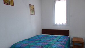A bedroom with a bed, a window, and a small wooden nightstand.