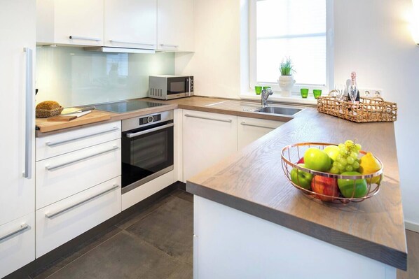 A modern kitchen with white cabinetry, a built-in oven, a microwave, and a wooden countertop. - Ferienhaus Strandhafer (Wangerooge)