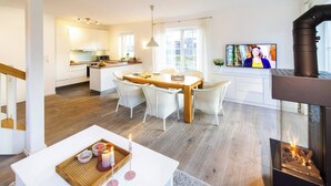 A modern living room with a dining area, a fireplace, and a kitchen in the background. - Ferienhaus Strandhafer (Wangerooge)