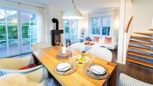 A dining area with a wooden table set for two, a fireplace, and a staircase leading to an upper level. - Ferienhaus Strandhafer (Wangerooge)