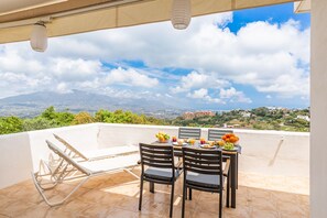 A terrace with a table set for breakfast, overlooking a scenic landscape with mountains and buildings.
