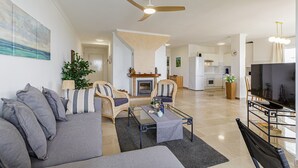 Een ruime woonkamer met een bank, fauteuils, een salontafel, een open haard en een televisie.